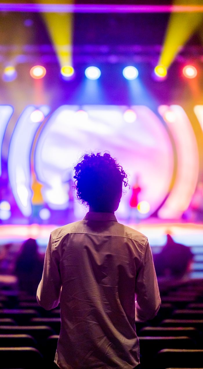 Back view of a man observing a vibrant stage with colorful lights and blurred background.