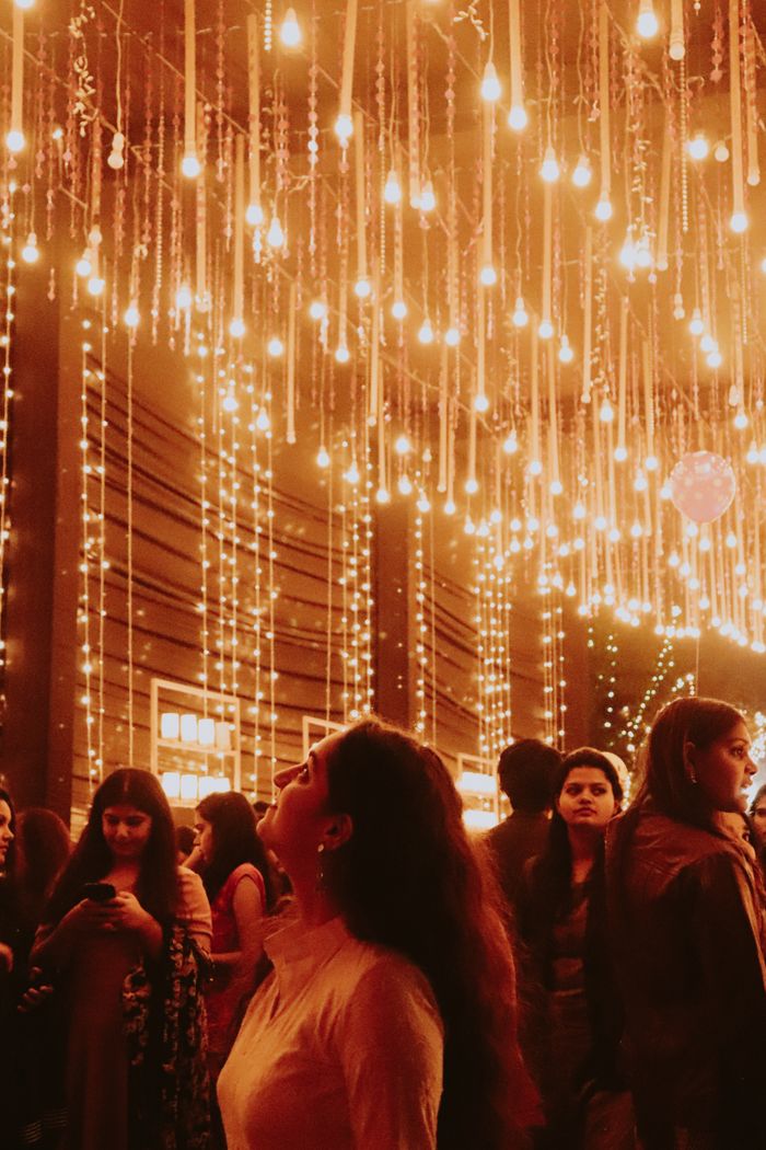 A woman gazing at hanging lights in a warmly lit indoor gathering.